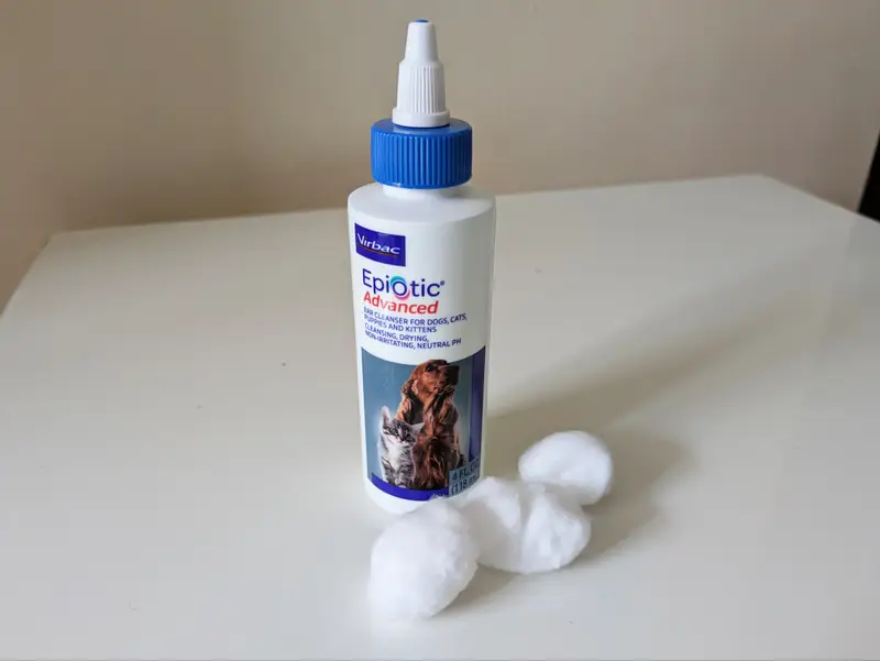 A bottle of dog-specific ear cleaning solution next to cotton rounds and a folded towel on a clean countertop