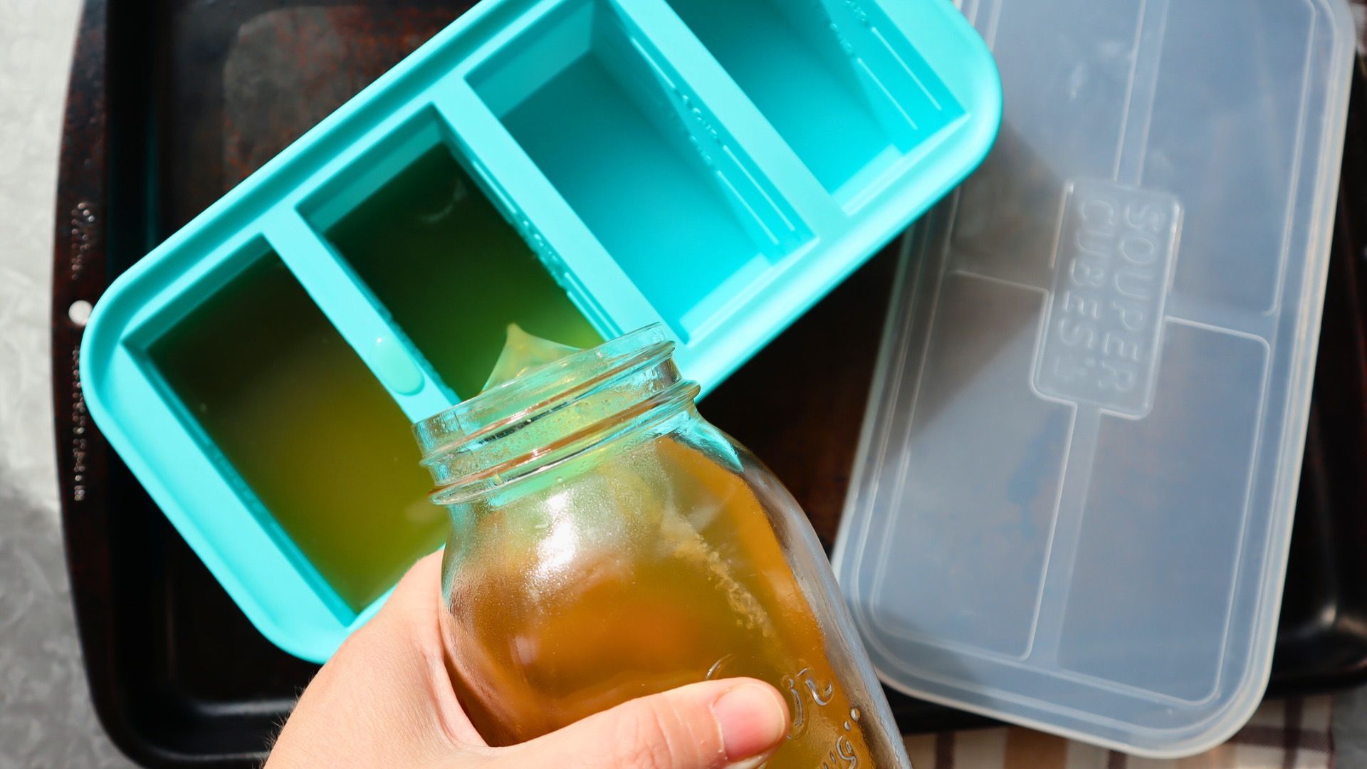 A silicone freezer tray filled with small cubes of plain homemade bone broth on a kitchen counter