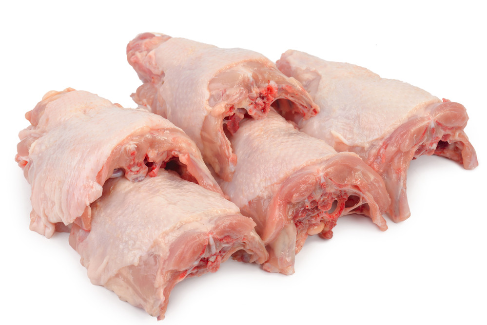 Raw chicken backs arranged next to a large stainless steel stockpot on a kitchen counter, ready to be cooked